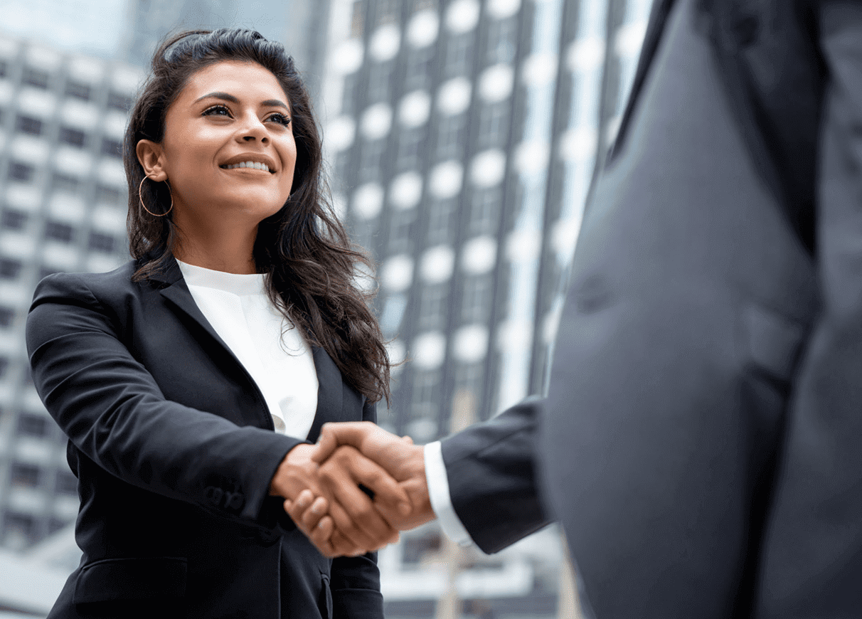 Two business professionals shaking hands in a city setting.